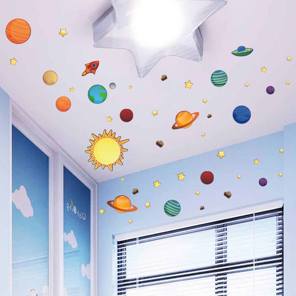 اتاق کودک با دیوارهای آبی و پرده کرکره ای که تزیین سقف آن با استیکرهای ماه و ستاره و سیاره های منظومه شمسی انجام شده است